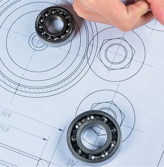 A person from DMI 3D, Inc. is holding a bearing on a blueprint.